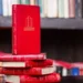 A stack of red hardcover books on a dark wooden shelf, representing Indian-American novels 2025