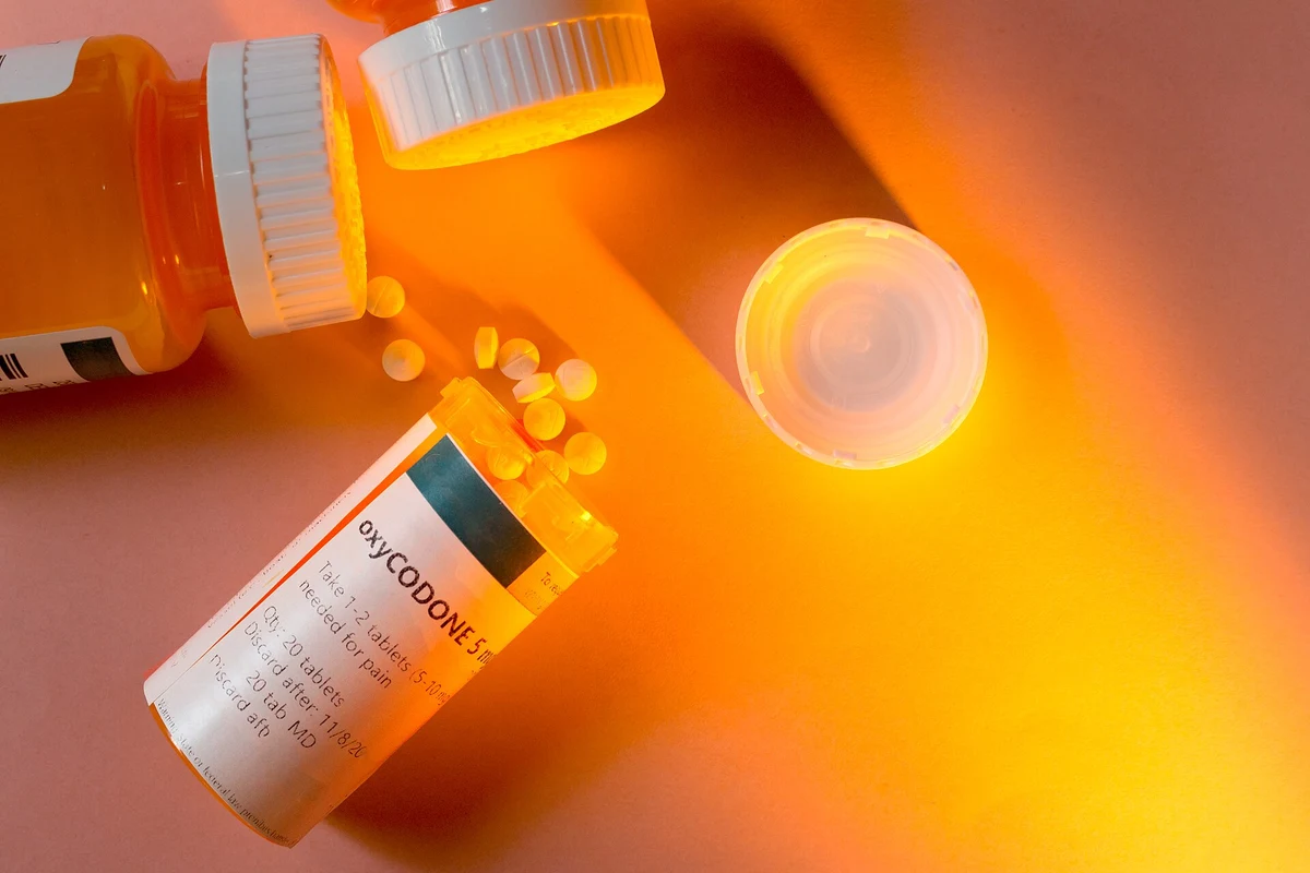 Oxycodone prescription bottle with tablets on an orange surface